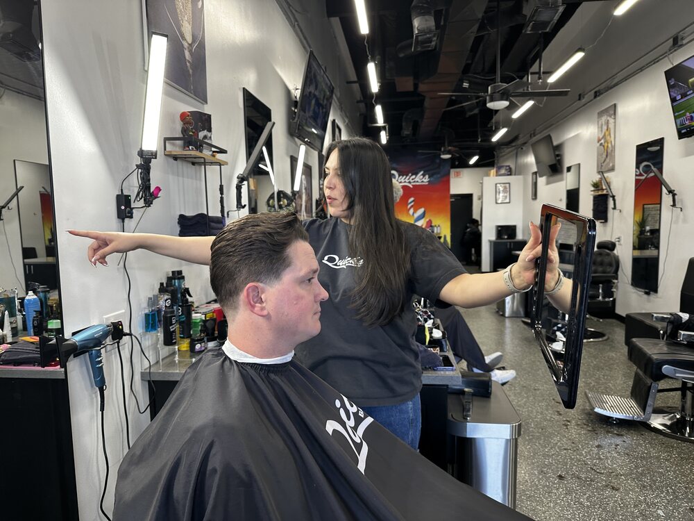 Gaby holding the mirror up to show a client the finished cut at Quicks Barbershop